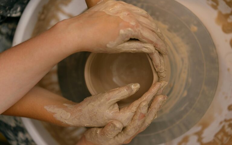 One pair of hands guiding another while making clay pottery