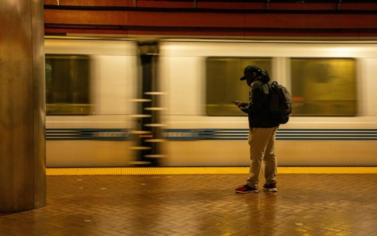 Man looking at his phone screen while a train passes by